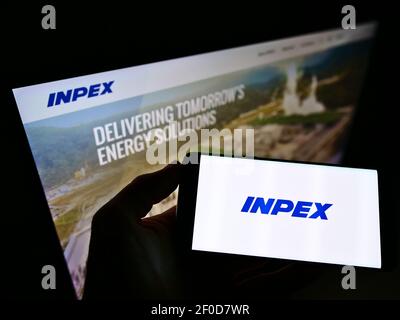 Personne tenant un smartphone avec le logo de la compagnie pétrolière japonaise Inpex Corporation à l'écran devant le site Web. Mise au point sur l'affichage du téléphone. Banque D'Images