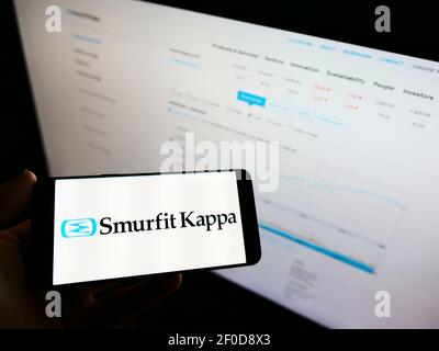 Personne tenant un téléphone portable avec le logo de la société irlandaise d'emballage Smurfit Kappa Group à l'écran devant la page web avec carte. Mise au point sur l'affichage du téléphone. Banque D'Images