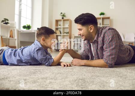 Le jeune père et son petit fils mignon se disputent des bras en étant allongé sur le sol. Banque D'Images