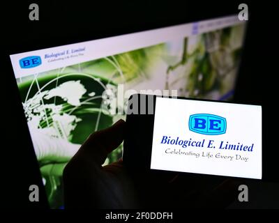 Personne tenant un téléphone portable avec le logo d'entreprise de la société indienne de vaccins Biological E. Limited à l'écran devant le site Web. Mise au point sur l'affichage du téléphone. Banque D'Images