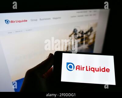 Personne tenant un smartphone avec logo de la société chimique française Air liquide S.A. sur écran devant le site. Mise au point sur l'affichage du téléphone. Banque D'Images