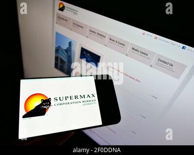 Personne tenant un téléphone portable avec le logo du producteur de gants malaisien Supermax Corporation Berhad à l'écran devant la page Web. Mise au point sur l'affichage du téléphone. Banque D'Images