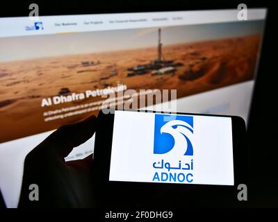 Personne tenant un téléphone portable avec le logo de la compagnie pétrolière nationale d'Abu Dhabi (ADNOC, pétrole et gaz) à l'écran devant la page Web. Mise au point sur l'affichage du téléphone. Banque D'Images