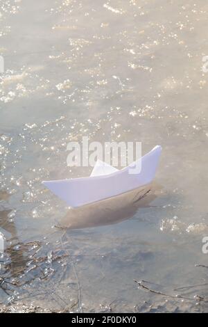 Bateau en papier blanc dans la flaque de glace du printemps. Concept début du printemps. Banque D'Images