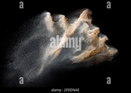 Explosion de sable isolée sur fond noir. Geler le mouvement des éclaboussures de poussière de sable. Banque D'Images