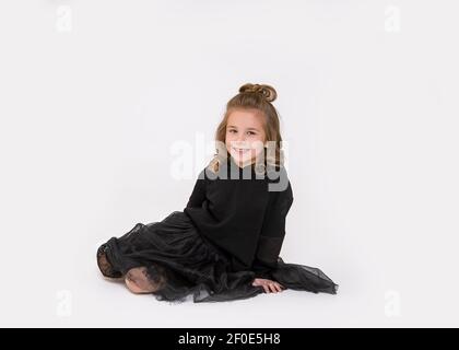 petite fille assise sur le sol en studio et regardant l'appareil photo sur fond blanc avec le sourire. Photo pleine longueur Banque D'Images
