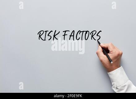 L'homme d'affaires écrit les facteurs de risque sur fond gris. Évaluation ou évaluation des risques dans le concept d'entreprise. Banque D'Images