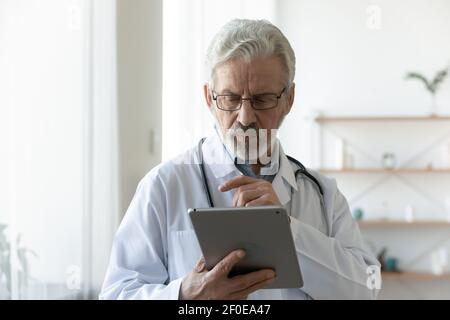 Un médecin mature et sérieux utilise un comprimé en clinique Banque D'Images