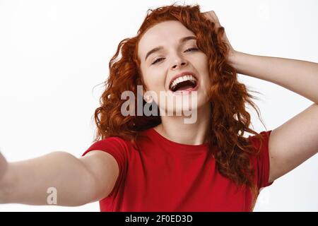 Portrait en gros plan d'une fillette au gingembre insouciante et heureuse, en touchant ses cheveux naturels et en riant tout en prenant le selfie, en tenant l'appareil photo à la main, prenez Banque D'Images