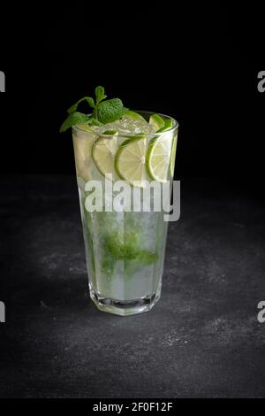 Mojito cocktail, avec de la glace, de la chaux et de la menthe, sur fond noir, sans entourage, vertical, faible profondeur de champ Banque D'Images