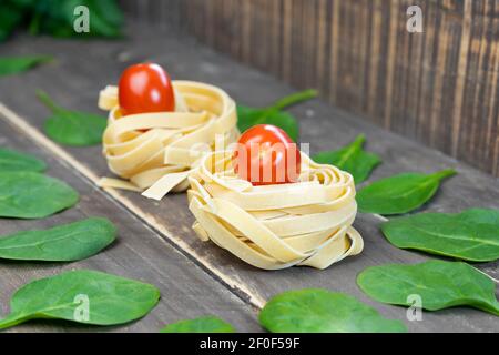 Tagliatelle de pâtes avec tomates cerises et feuilles d'épinards sur fond de bois.régime sain, concept propre de style de vie de nourriture . Banque D'Images