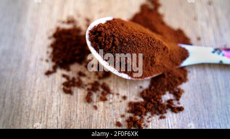 Poudre de café dans le cuillère isolée sur fond de table en bois. Pile de café brun qui déborde sur le sol, vue du dessus, épices indiennes Banque D'Images