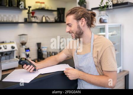 Homme souriant dans le profil vérifiant les factures dans le café Banque D'Images