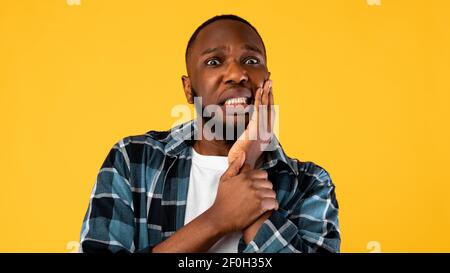 Black effrayé Guy touchant la joue ayant mal de dents sur fond jaune Banque D'Images