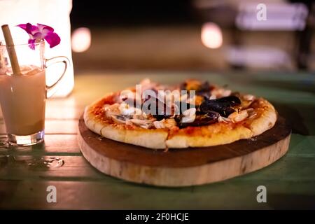 pizza avec fruits de mer sur une table dans un café, à côté d'un cocktail avec une fleur d'orchidée, un délicieux dîner sur la mer, fond flou Banque D'Images