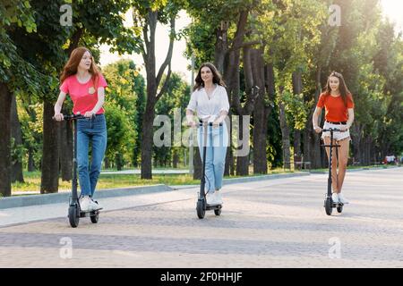 Trois jeunes filles amis sur les trottinettes d'avoir du plaisir dans la rue de ville à l'été ensoleillé jour. Portrait extérieur de trois amis fille à cheval électrique Banque D'Images