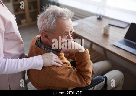 Portrait d'un homme seul âgé en fauteuil roulant à la maison de retraite avec une infirmière qui le réconforte, espace de copie Banque D'Images