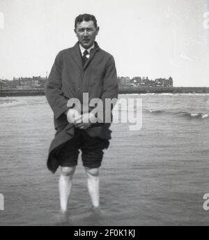 Années 1950, historique, un homme dans son costume et son manteau, ayant une pagaie dans l'eau de mer peu profonde à Cleethorpes, avec son pantalon roulé vers le haut, Angleterre, Royaume-Uni. Petite ville de bord de mer sur l'estuaire de la rivière Humber dans le nord-est de l'Angleterre, c'était à l'origine un village de pêcheurs, avant de se développer dans une station avec sa longue plage de sable et les offres britanniques plus traditionnelles d'arcades d'amusement et de manèges à ânes. Banque D'Images