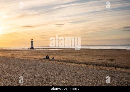 Une famille s'est assise toute seule sur une grande propreté déserte vacances à la plage d'observation du coucher du soleil avec phare et l'heure d'or magnifique orange ciel d'été Banque D'Images