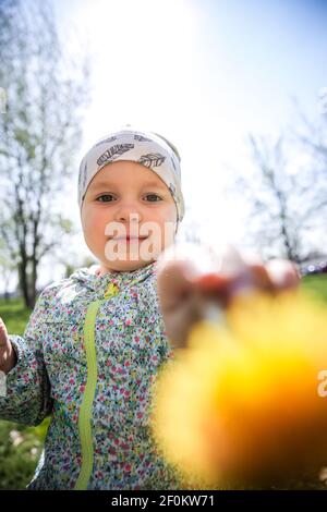 Petite fille souriante assise sur l'herbe et tenant jaune pissenlits Banque D'Images