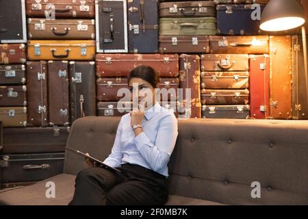 Femme d'affaires indienne réfléchie tenant une tablette, assise sur un canapé, méditer sur une stratégie Banque D'Images