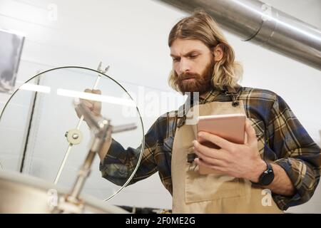 Portrait à angle bas d'un brasseur à bière barbu inspectant la production à l'usine de fabrication de bière, espace de copie Banque D'Images