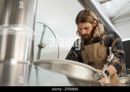 Portrait à angle bas d'un brasseur à bière barbu contrôlant la production à l'usine de fabrication de bière, espace de copie Banque D'Images