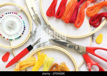 Accessoires de broderie sur toile de lin blanche. Cerceau à broderie, fils, aiguille et ciseaux. Couleur rouge et jaune Banque D'Images