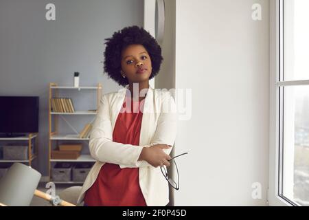 Femme afro-américaine pensive de bureau debout et regardant appareil photo Banque D'Images