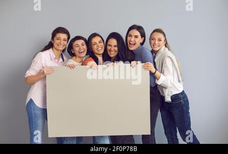 Groupe de femmes heureuses debout en studio, riant et tenant une bannière en carton vide Banque D'Images