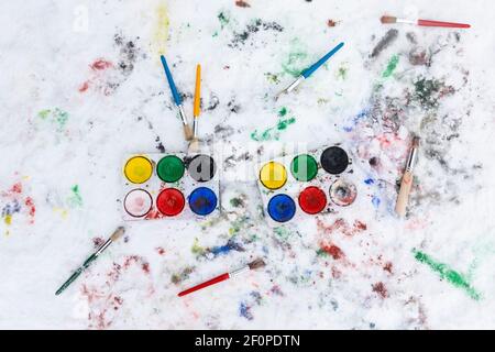 Peinture aquarelle sur la neige en plein air. Deux boîtes de peinture couleur eau et des pinceaux épars vus de dessus. Il y a de la peinture sur la neige. En plein air Banque D'Images