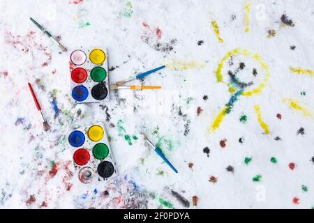 Peinture aquarelle sur la neige en plein air. Deux boîtes à peinture et pinceaux de couleur eau sont vus de dessus. Il y a de la peinture sur la neige et un happ peint Banque D'Images