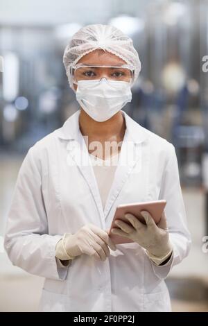 Portrait vertical de la taille vers le haut de la jeune femme travaillant à un produit chimique plante et regarde la caméra tout en portant des vêtements de protection Banque D'Images