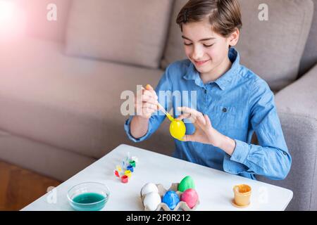 Une jeune fille de neuf ans en chemise bleue peint des œufs à une table blanche. Concept de Pâques. Mise au point sélective. Banque D'Images