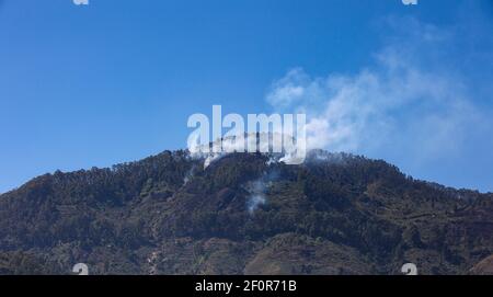 Fumée émise par un sommet de montagne en raison de la barre oblique et brûlez l'agriculture pratiquée par les villageois tribaux comme vu en voyageant Sur Palani Ghat Road Banque D'Images