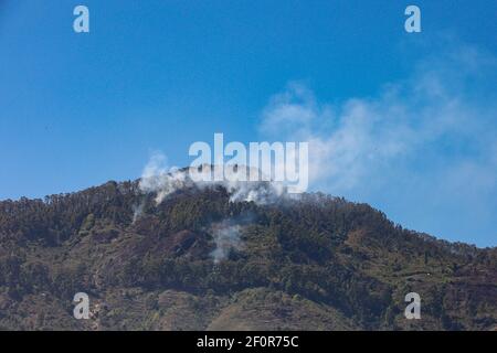 Fumée émise par un sommet de montagne en raison de la barre oblique et brûlez l'agriculture pratiquée par les villageois tribaux comme vu en voyageant Sur Palani Ghat Road Banque D'Images