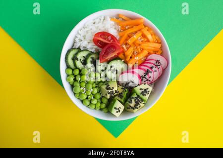 Bol à poke végétalien avec du riz blanc et des légumes dans le bol blanc au centre de l'arrière-plan coloré.vue du dessus.gros plan. Banque D'Images