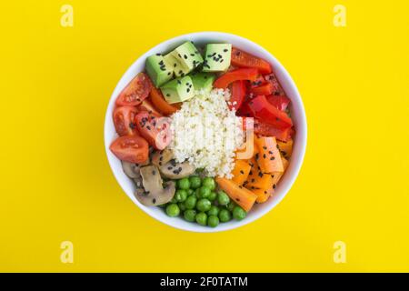 Bol à poke végétalien avec couscous et légumes dans le bol blanc au centre du fond jaune. Vue de dessus. Copier l'espace. Gros plan. Banque D'Images