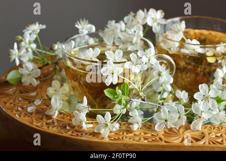 Thé de fleur de cerisier dans une tasse de verre avec des branches florales en fleur à proximité, la boisson saine de fines herbes est bon pour la peau et le coeur, riche en antioxydants et l'esse Banque D'Images