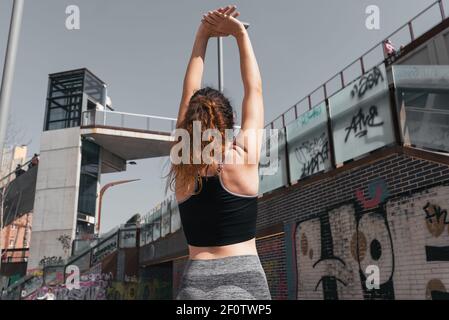 Jeune femme de derrière, portant un haut de sport et des leggings, étirant les deux bras au-dessus de sa tête Banque D'Images