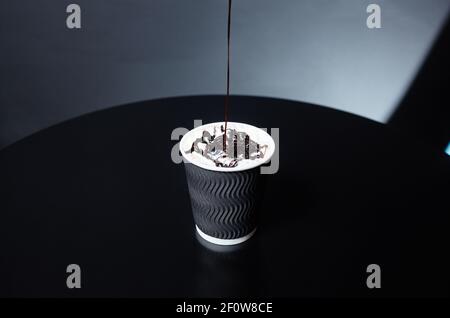 Le barista met du chocolat liquide sur la crème fouettée dans une tasse en papier jetable. Processus de fabrication de boisson savoureuse au café avec du lait, de la crème et du chocolat Banque D'Images