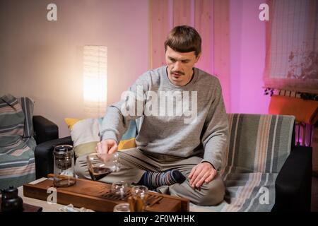 Un jeune homme boit un délicieux thé chinois noir aromatique dans un bol en verre lors d'une authentique cérémonie de thé à la maison. Banque D'Images