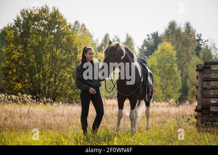 Marcher une fille avec un cheval le long de la clôture à le ranch à l'automne Banque D'Images