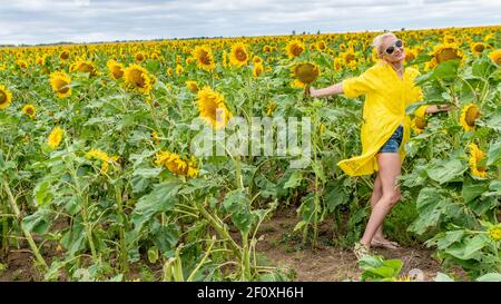 Belle femme dans une robe jaune avec une apparence charismatique sur le fond d'un champ de tournesol bleu nuages pendant le jour et l'été Banque D'Images