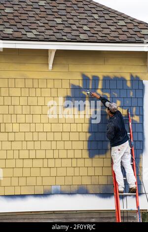 Atlantic City, NJ - 27 octobre 2020: Homme sur une échelle rouge appliquant de la peinture bleue avec un pistolet à pulvérisation à un bâtiment jaune. Banque D'Images