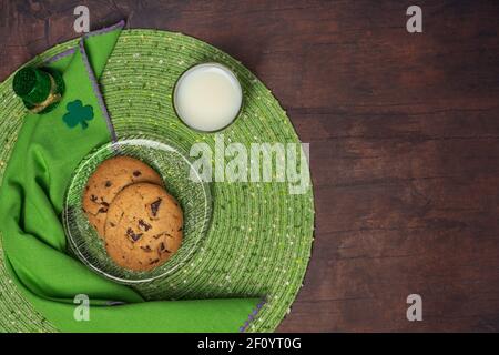 Le jour de la Saint-Patrick, régalez-vous de biscuits et de lait sur une assiette en verre avec un napperon, une serviette, un shamrock et un petit chapeau de leprechaun sur un fond de table en bois Banque D'Images