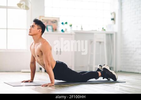 Un jeune homme asiatique musclé fait des exercices sur le sol à la maison Banque D'Images