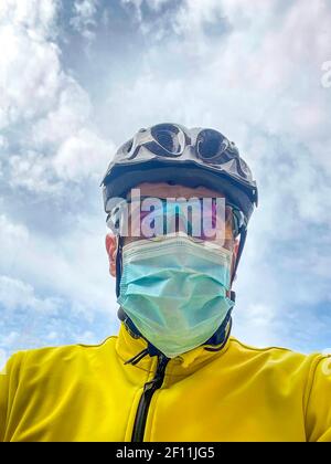 portrait d'un cycliste portant un casque, des lunettes et une veste jaune, portant un vélo avec un masque, portrait vertical contre un ciel nuageux Banque D'Images