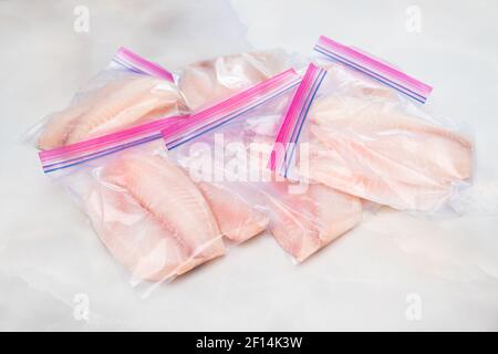 Filet de poisson frais dans des sacs à fermeture à glissière. Filet de tilapia sur fond de marbre clair, vue rapprochée du dessus Banque D'Images
