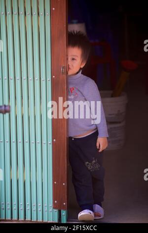 Un garçon vietnamien pieurant derrière les volets du magasin, bac Ha, province Lao Cai, Vietnam. Banque D'Images